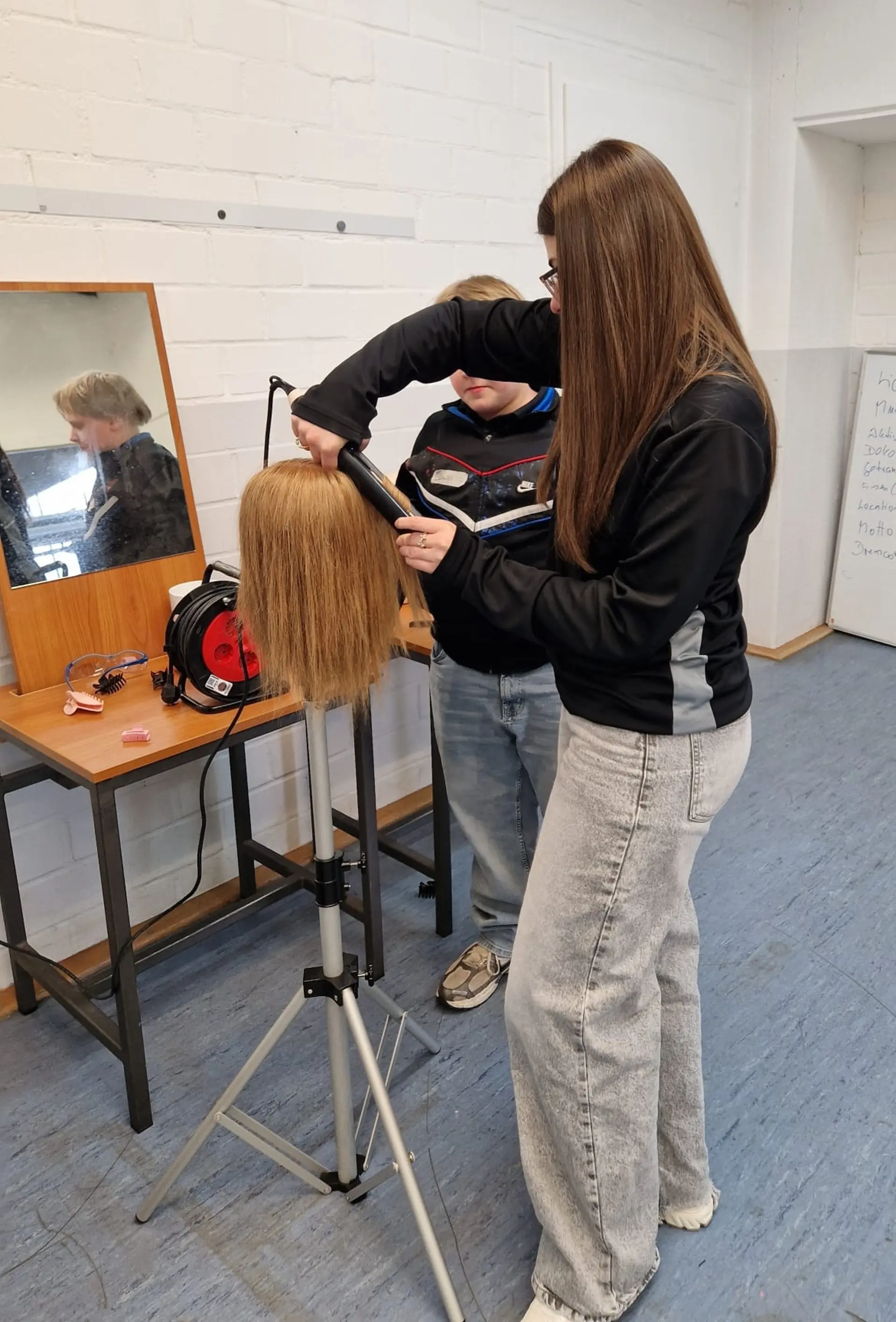 Schülerinnen frisieren Kopfhaar an einer Puppe
